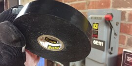 Gloved hand holding roll of Scotch® Vinyl Electrical Tape Super 88 in front of electrical switch