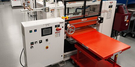 Image of a roll coater with a feed table and control box
