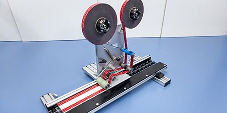 Image of a push-through laminator that applies two parallel strips of tape to a metal bar

