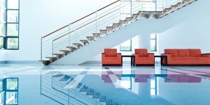 Instalación con escaleras marrones, tres sillones color ladrillo y piso brillante azul.
