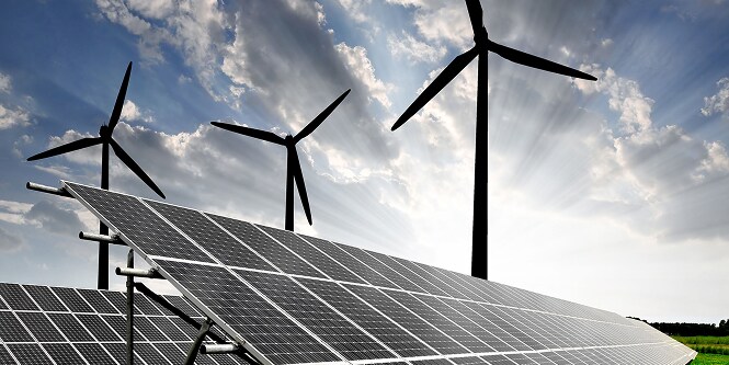 Paneles solares en primer plano y tres turbinas eólicas al fondo bajo un cielo parcialmente nublado, representando generación de energía renovable.
