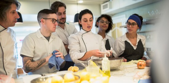 Un grupo de cocineros en una cocina alrededor de una mujer.

