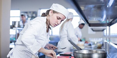 Una mujer con gorro de chef cocinando en una cocina.
