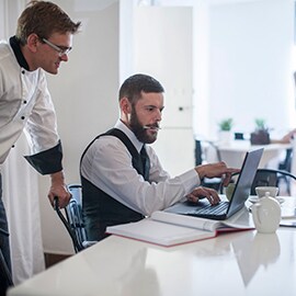 A chef and an administrator look at a laptop computer in an upscale restaurant.