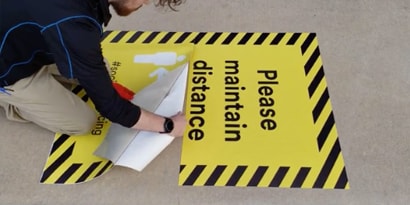 Trabajador de 3M colocando un gráfico cuadrado sobre una acera de concreto.

