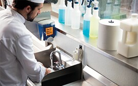 male chef washing his hands with disinfectant bottles displayed in background.