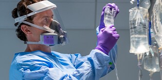 Clinician wearing a half facepiece reusable respirator checking an IV
