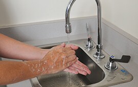 close up of soapy hands being washed with hot water under a commercial sink