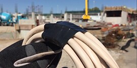 gloved hand holding roll of Scotch® Vinyl Electrical Tape Super 88 wrapped on cable at construction site