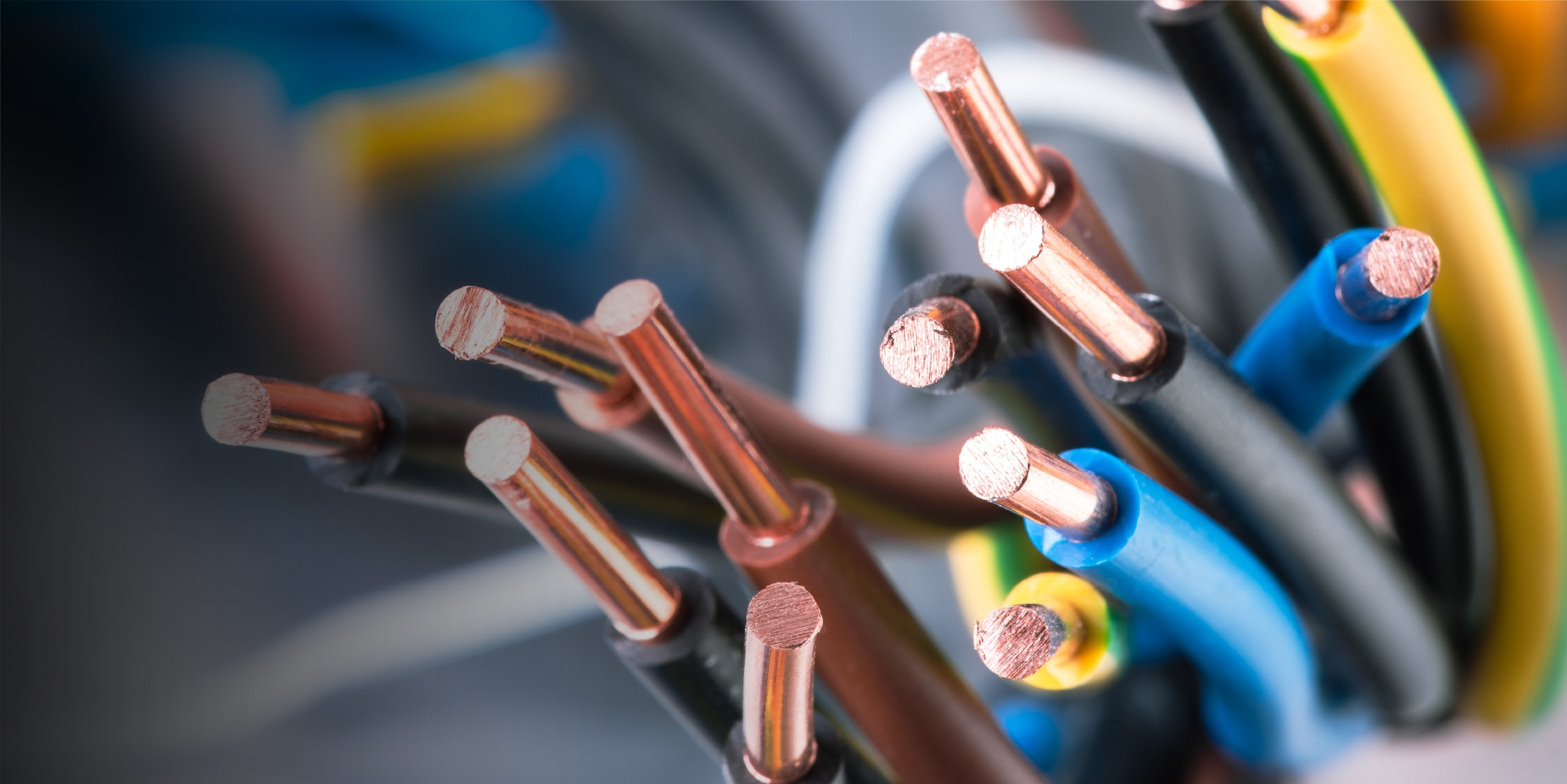 Primer plano de varios cables eléctricos con puntas de cobre expuestas y aislamientos de diferentes colores, incluyendo azul, amarillo, negro y marrón, agrupados en conjunto.
