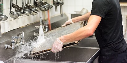 dishwasher cleaning a pan at a commercial sink in the back of the house.
