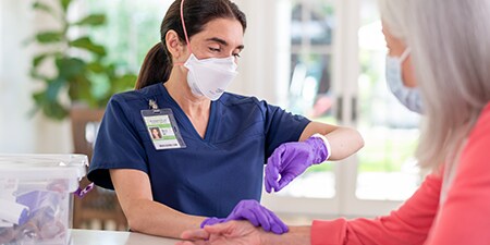 Clinician wearing a filtering facepiece respirator checking a patient’s pulse
