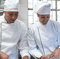 Dos chefs con batas blancas conversan en una cocina comercial.