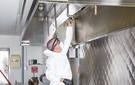 man wearing a hazmat suit disinfecting commercial cooking hood ranges.