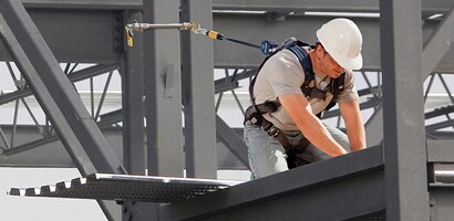 Worker kneeling on beam connected to fall protection anchor
