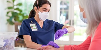 Clinician wearing a filtering facepiece respirator checking a patient’s pulse
