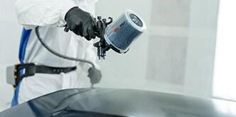 Técnico de pintura pulverizando vehículo.
