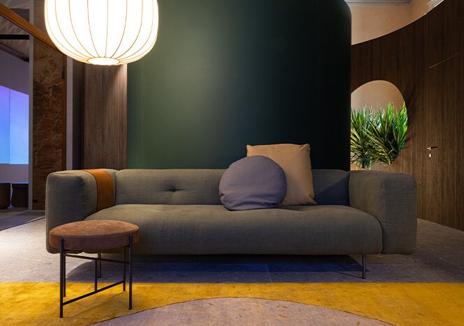 Salón redondo con pared acabada en madera oscura y columna verde mate con un sofá gris centrado en el marco.